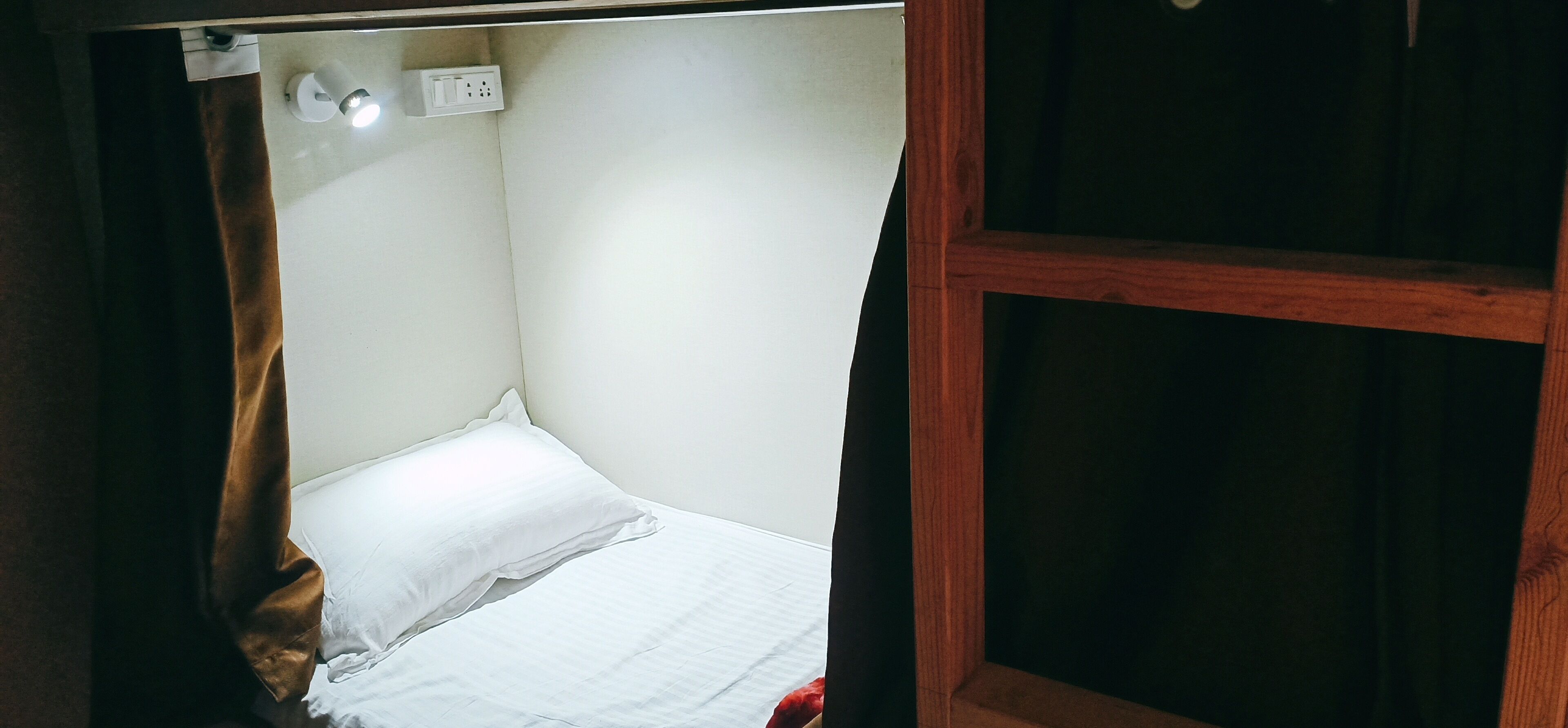Une petite chambre avec un lit simple, une tête de lit en bois, un mur blanc et une prise de courant située au-dessus du lit.