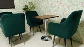 Une pièce avec un papier peint à motifs floraux, une petite table et trois chaises vertes.