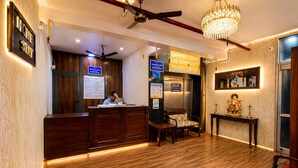 Un hall d’accueil d’hôtel avec un bureau en bois, un comptoir d’accueil, un lustre et un panneau indiquant qu’il s’agit d’un établissement d’hébergement privé.