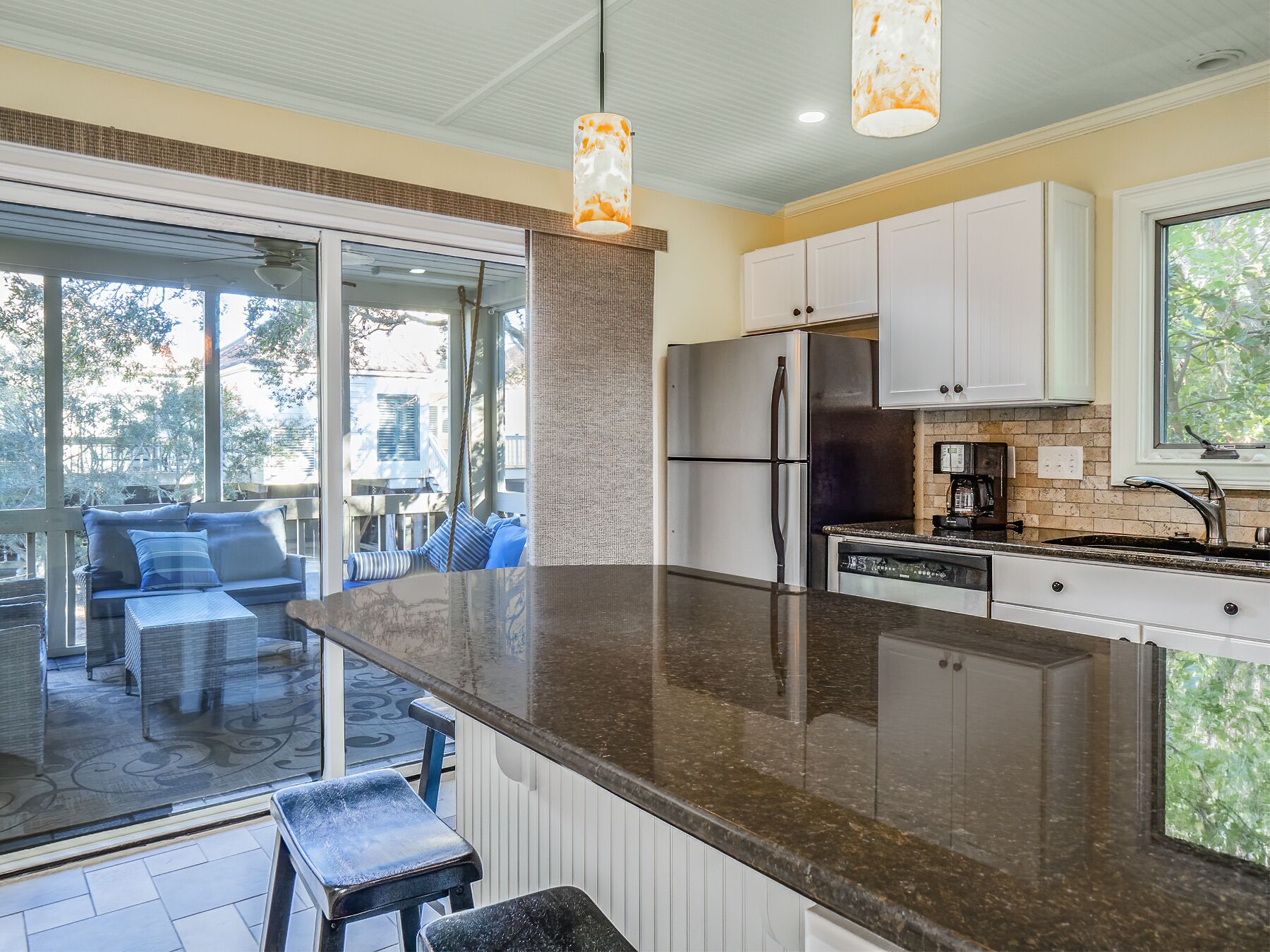 Una cocina moderna con una isla grande, electrodomésticos de acero inoxidable y un puerta corrediza de vidrio que da a un patio con mobiliario exterior.