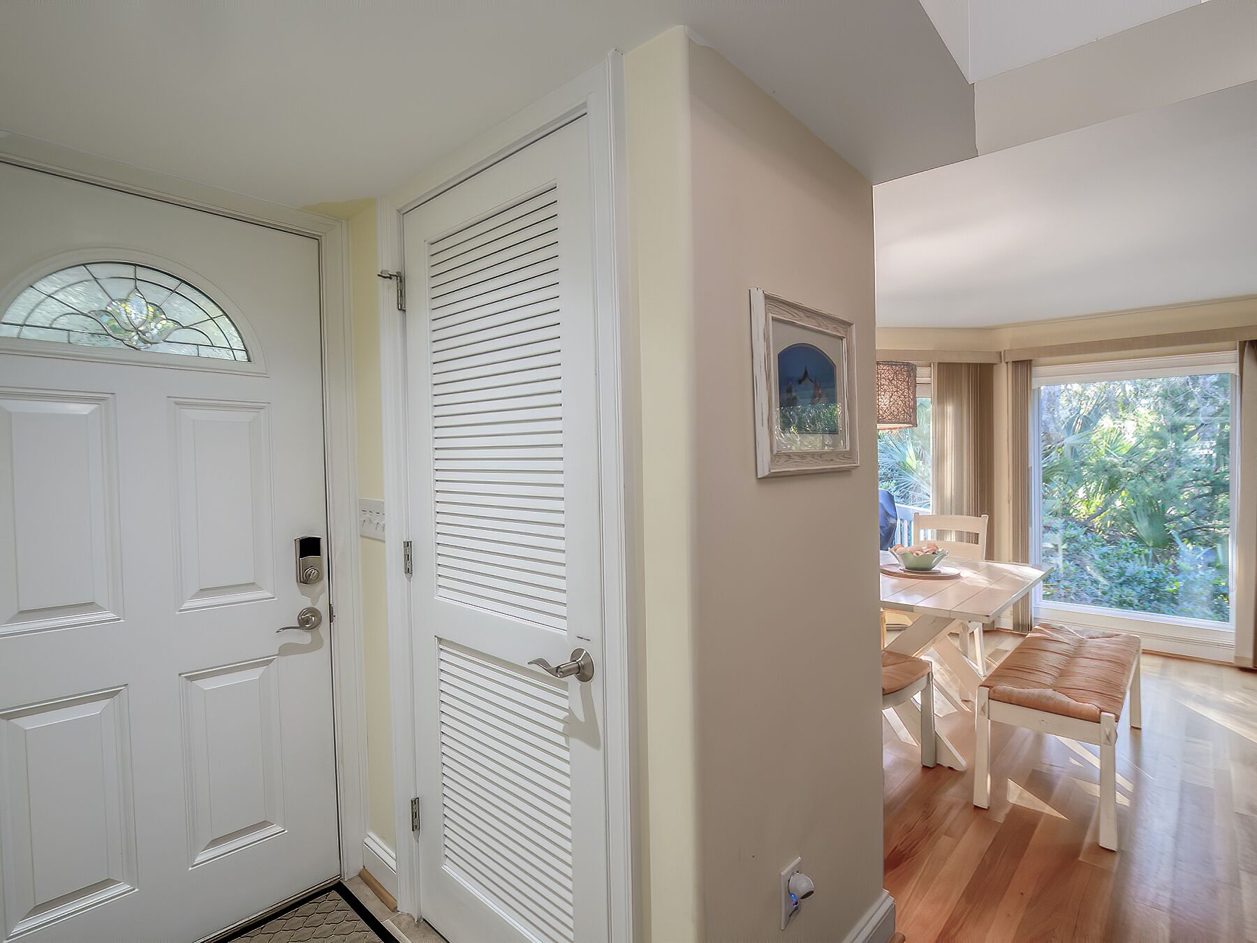 A hallway with a white door, a window with a stained glass design, and a dining area with a table and chairs.