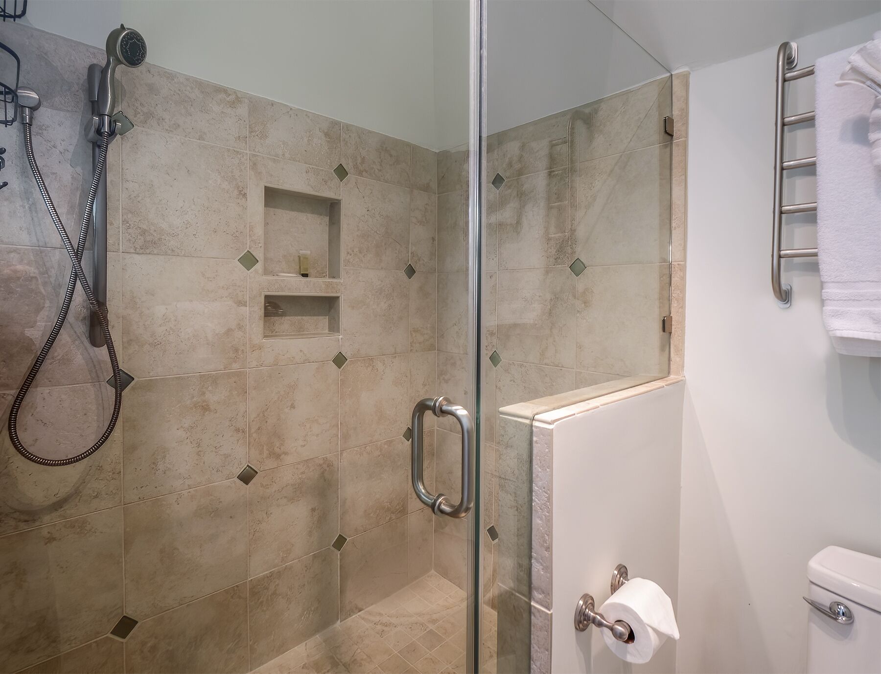 Une salle de bain moderne dotée d’une douche à parois de verre, de toilettes avec un porte-serviettes en papier et d’un porte-serviettes.