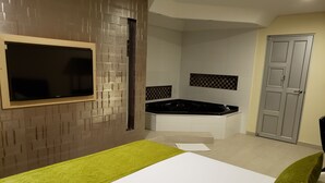 Un dormitorio moderno con una cama grande, un televisor montado en la pared, una bañera integrada y un armario.