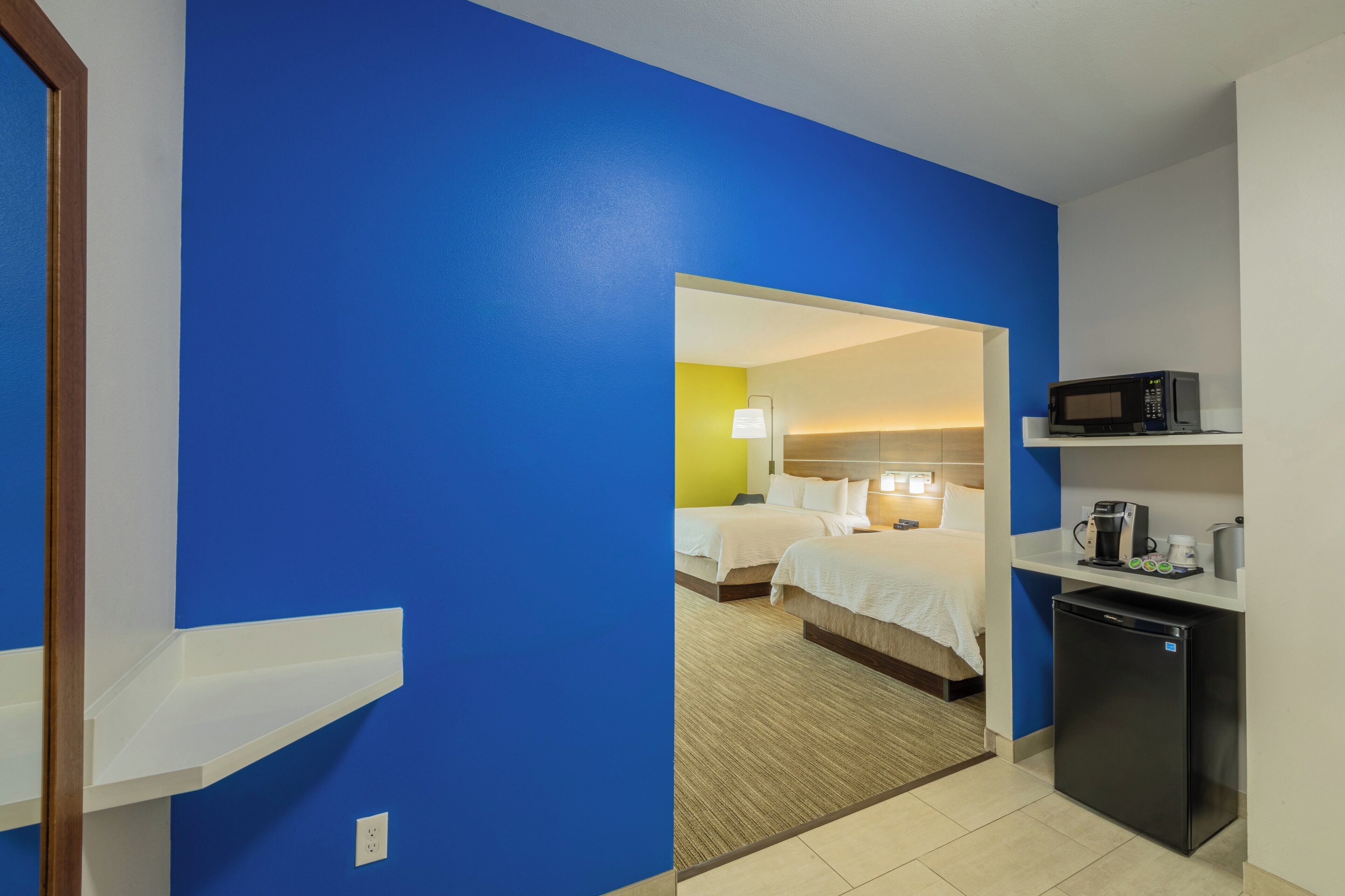 Hotelkamer met een blauwe muur, een bed, een bureau met een magnetron en een koelkast.