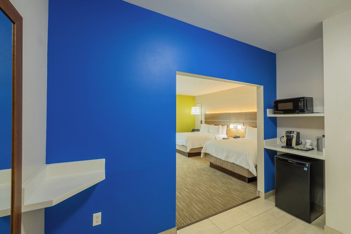 A hotel room with a blue wall, a bed, a desk with a microwave, and a refrigerator.