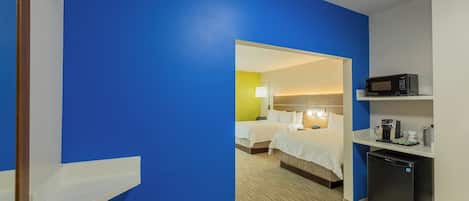 A hotel room with a blue wall, a bed, a desk with a microwave, and a refrigerator.