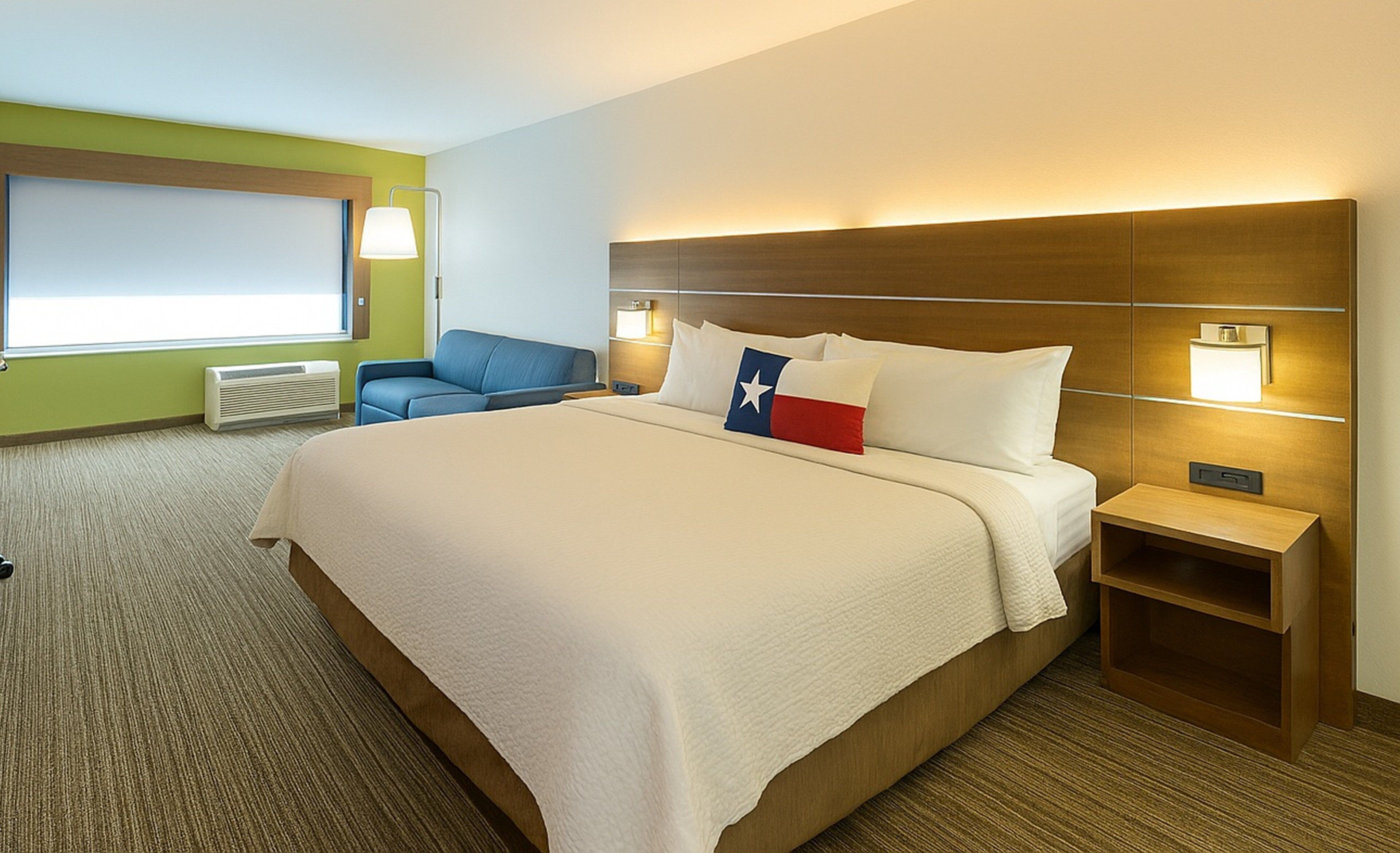 Ein Hotelzimmer mit einem großen Bett, einem Schreibtisch, einem Stuhl, einem Nachttisch, einer Lampe und einem Fenster mit Jalousien.