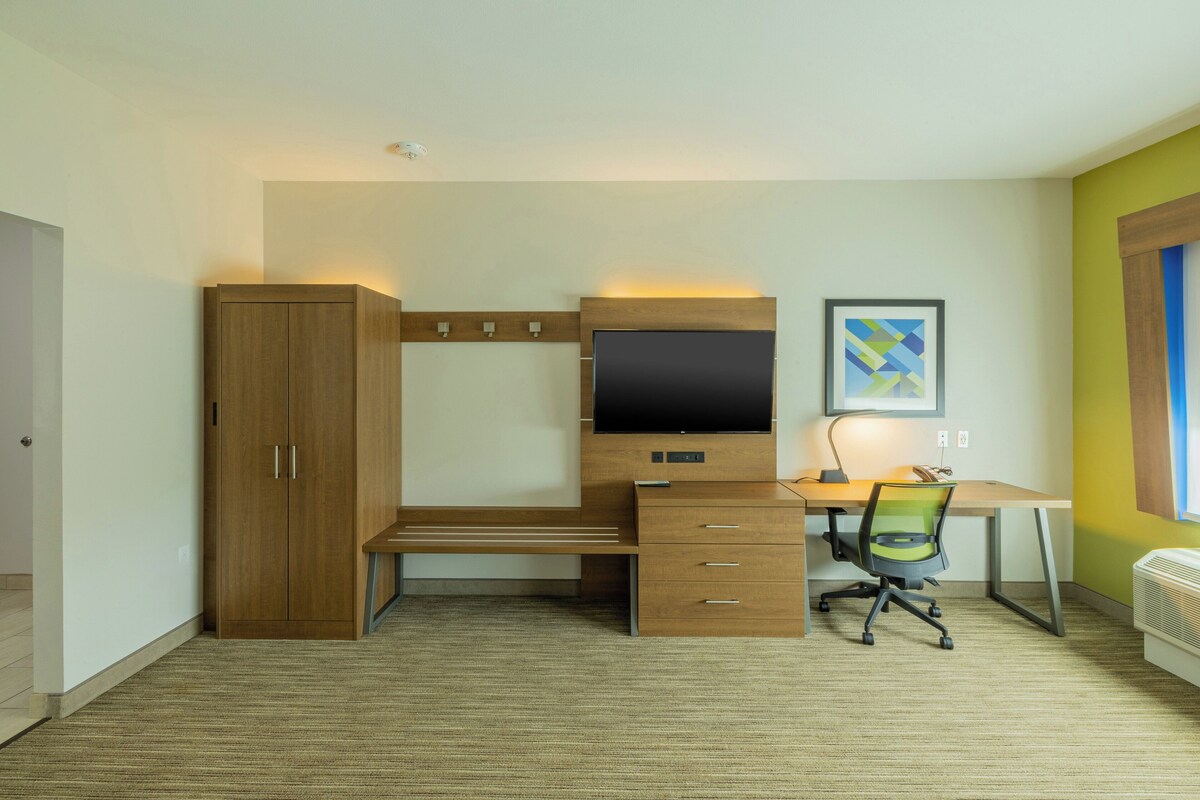 A bedroom with a bed, a wardrobe, a desk with a computer, and a chair.