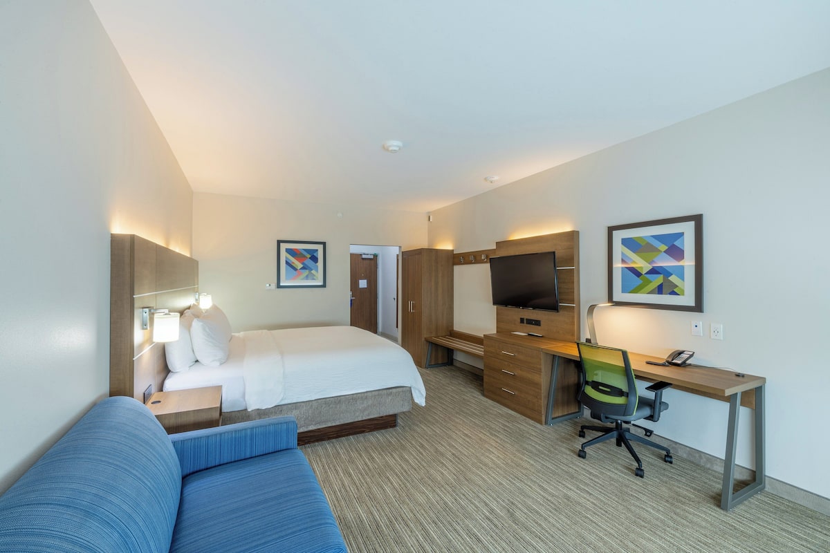 Ein Hotelzimmer mit Bett, Schreibtisch, Stuhl, Fernseher und Bildern an den Wänden.