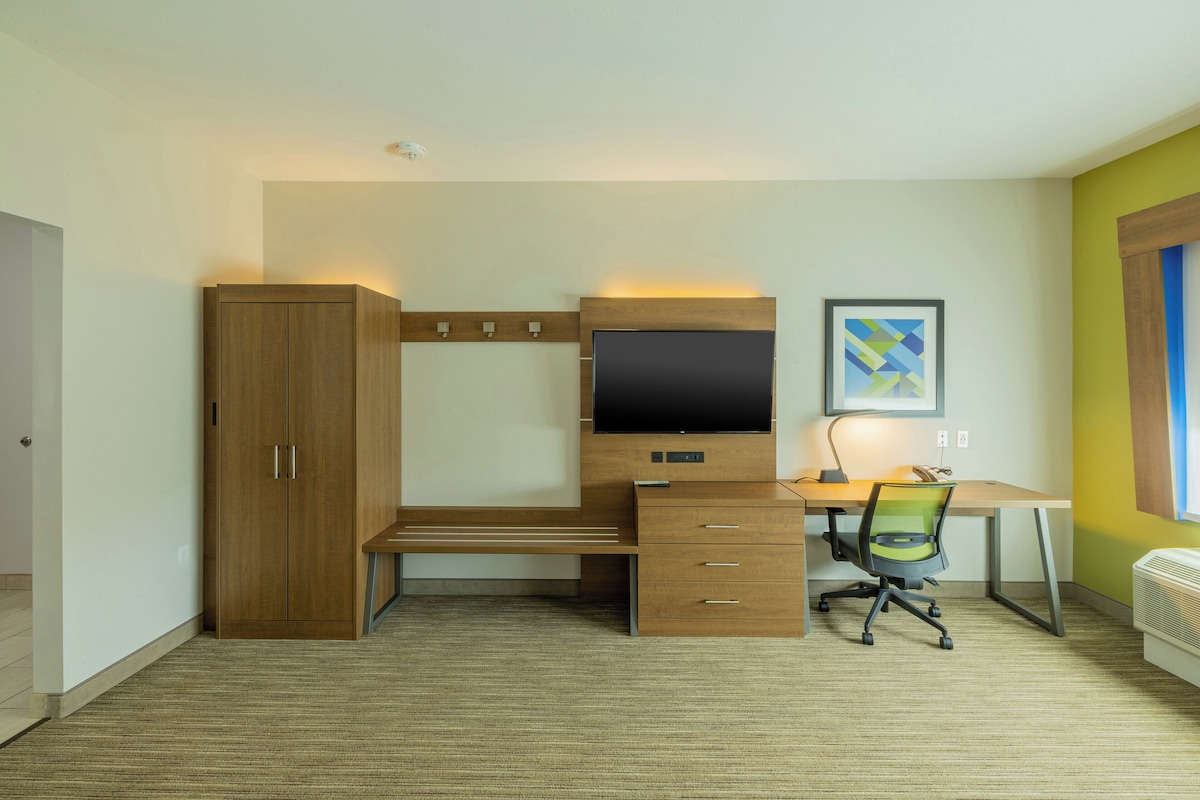 Een slaapkamer met een bed, een kledingkast, een bureau met een computer en een stoel.