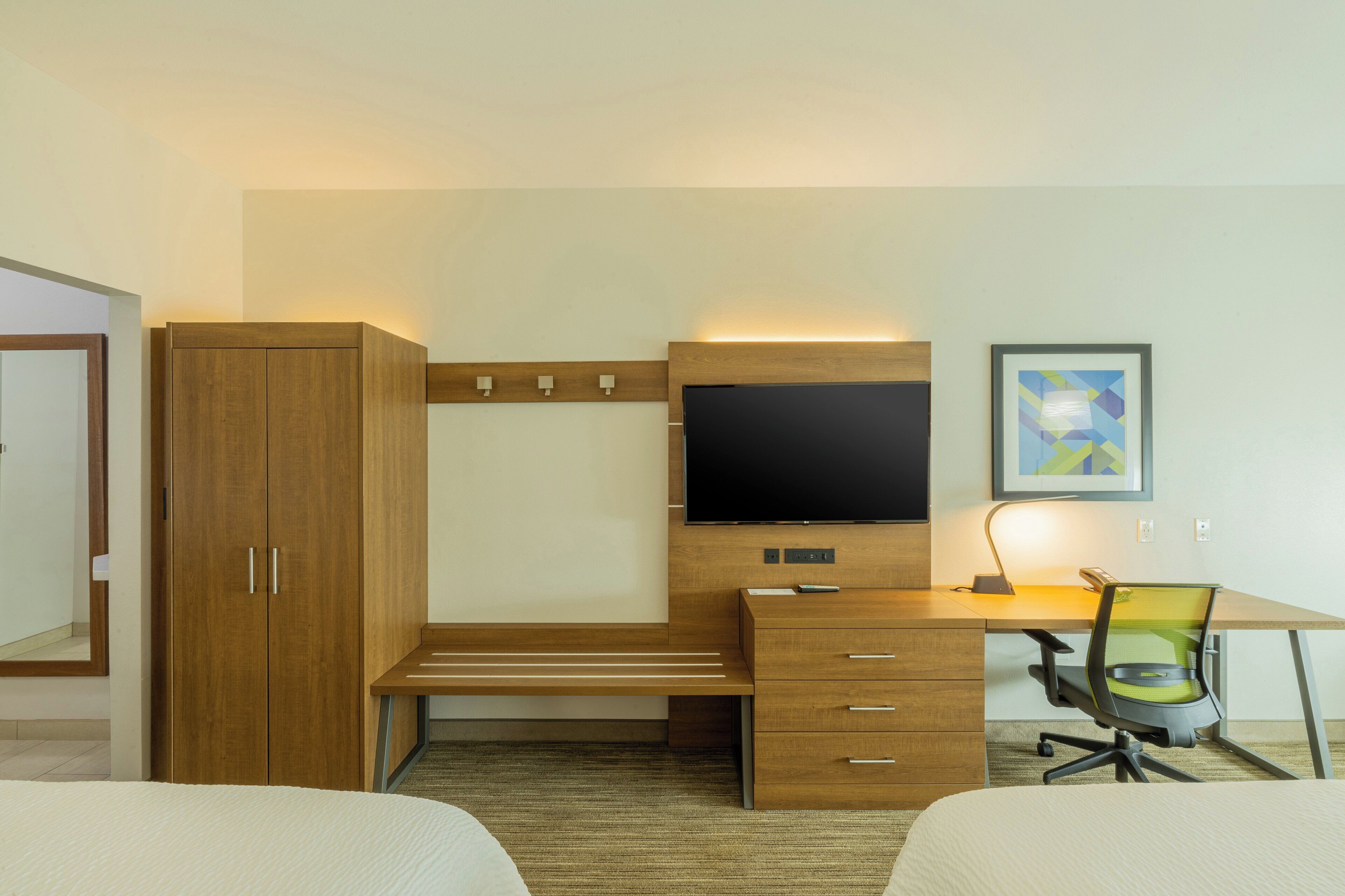 A hotel room with a wooden wardrobe, a desk with a chair, a television, and a framed picture on the wall.
