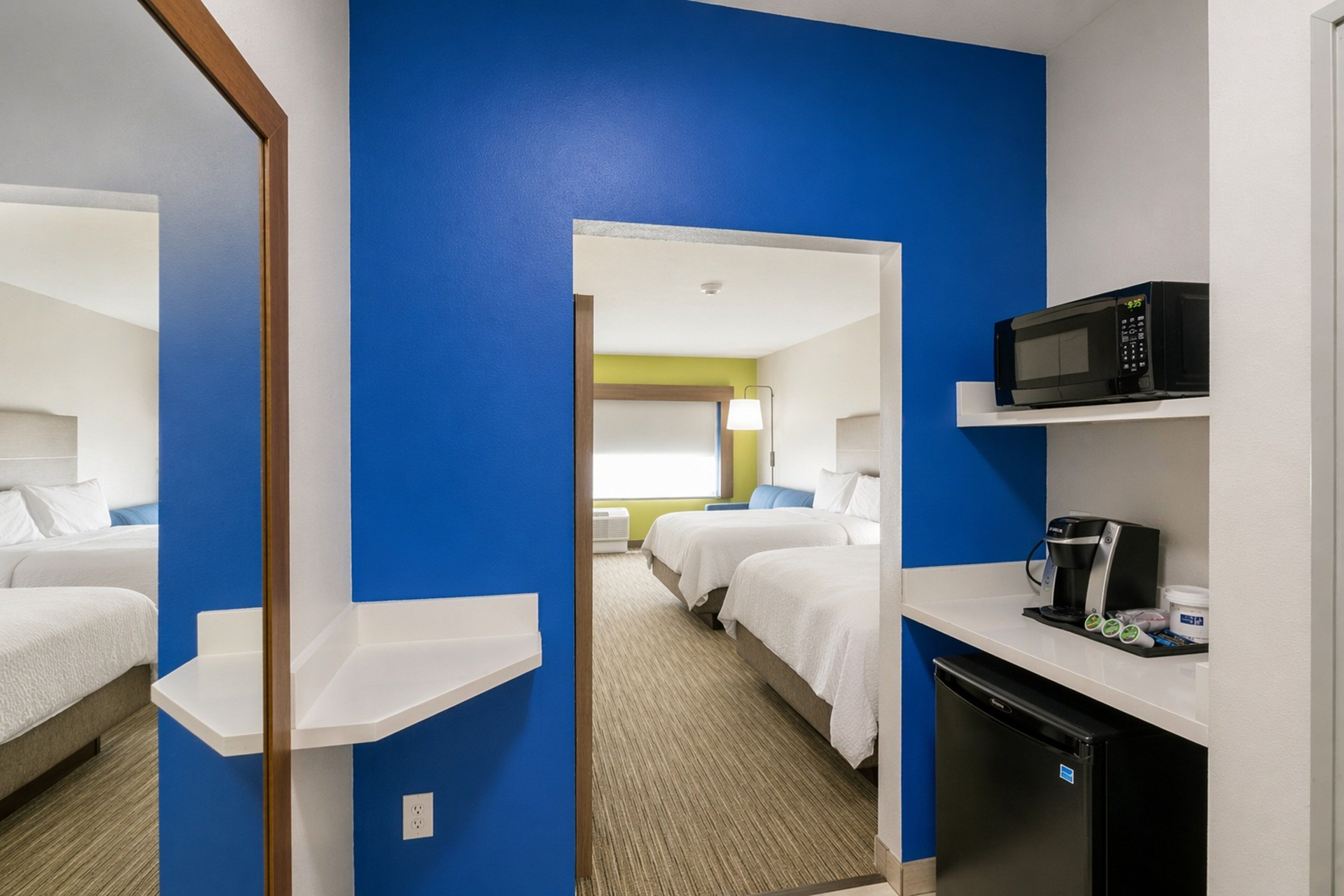 A hotel room with a blue accent wall, a bed, a desk with a microwave, and a coffee maker.
