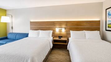 A hotel room with two beds, a nightstand, a lamp, and a wall-mounted light.