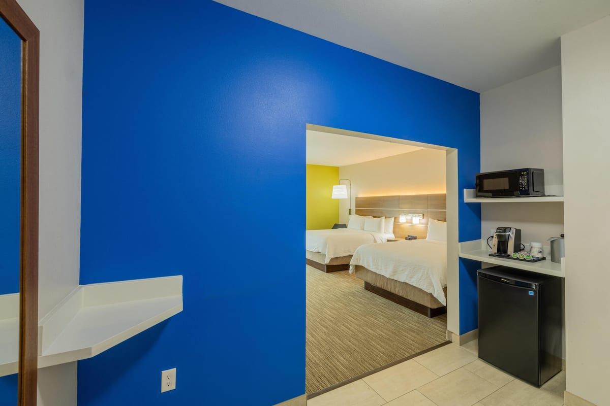 A hotel room with a blue accent wall, a bed, a desk with a microwave, and a refrigerator.