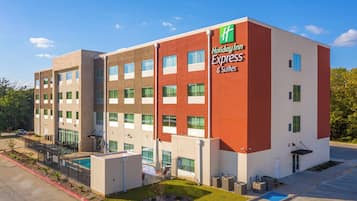 Un hotel Holiday Inn Express & Suites con un diseño moderno, que presenta fachada roja y blanca, numerosas ventanas y una zona de piscina.