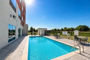 A swimming pool with a clear blue water, surrounded by a deck area with chairs and tables, and a building with large windows and a sign indicating pool rules. - Holiday Inn Express & Suites Lindale – Tyler by IHG (Lindale)