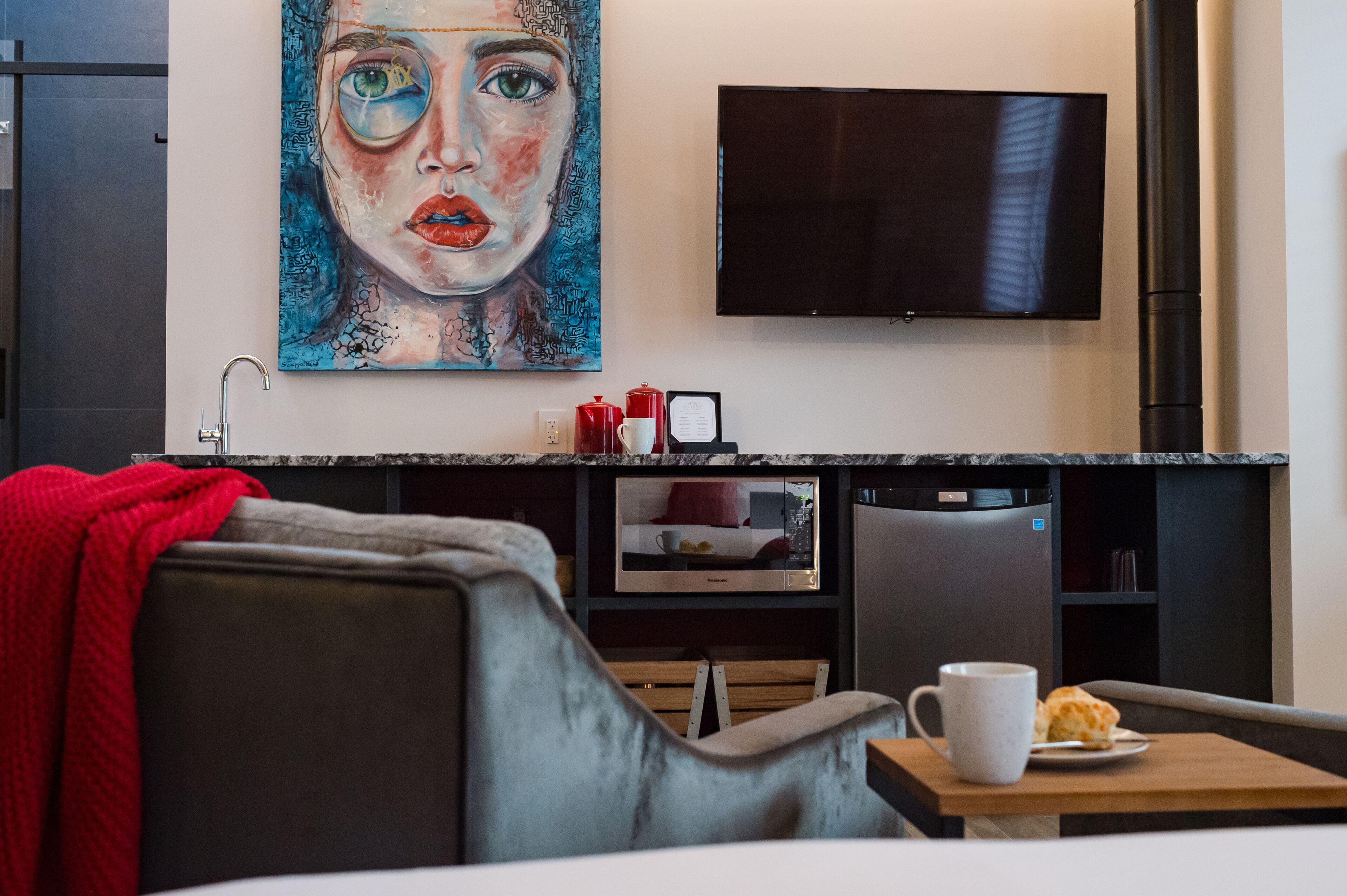 Una sala de estar moderna con un sofá, una mesa de centro con una taza y una galleta, un televisor de pantalla plana y un cuadro en la pared.