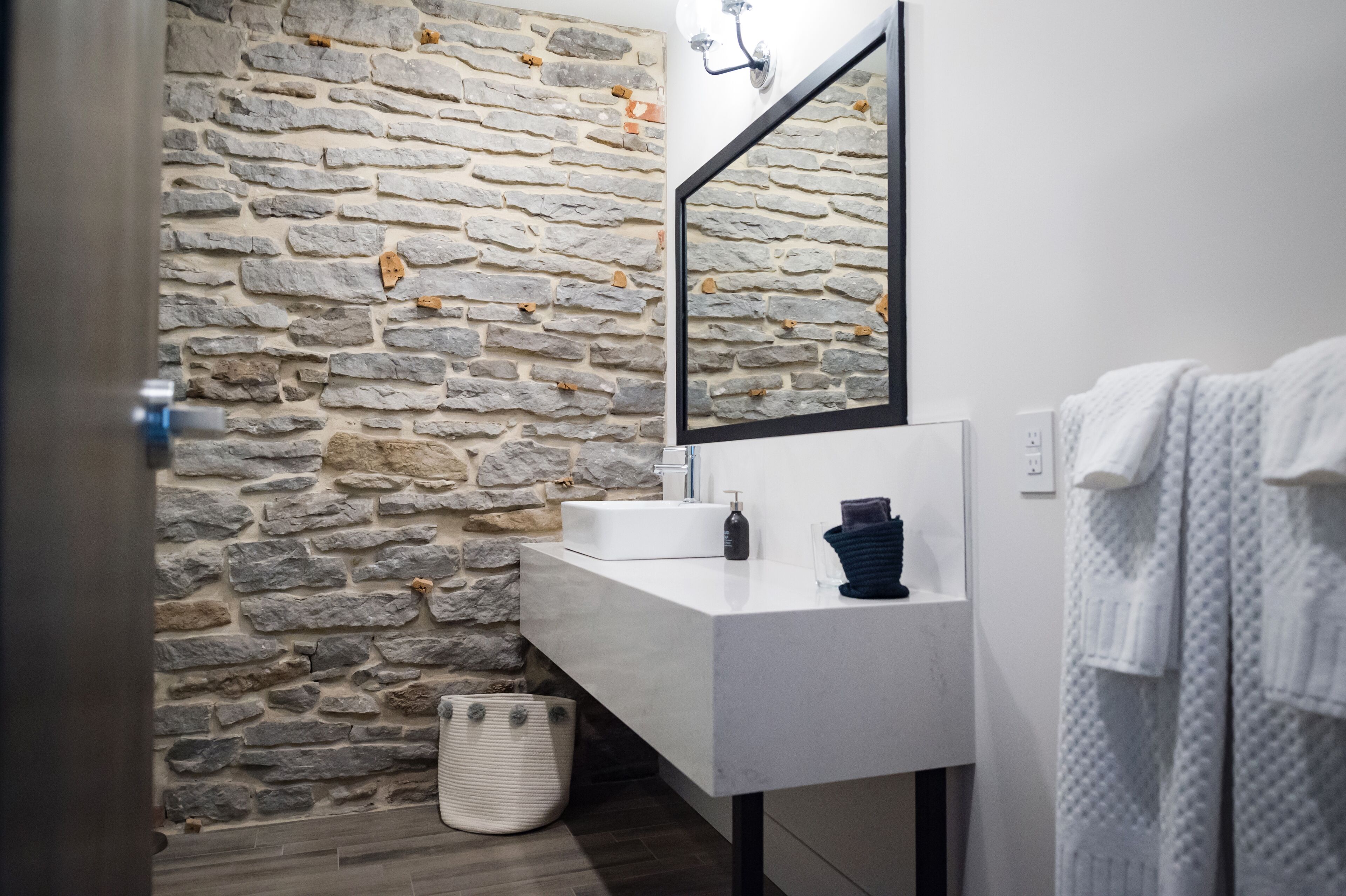 A bathroom with a stone wall, a white sink, a mirror, and a towel rack.