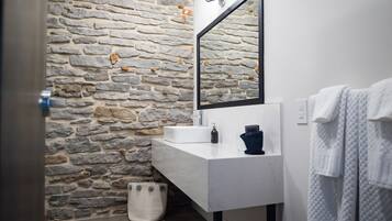 A bathroom with a stone wall, a white sink, a mirror, and a towel rack.