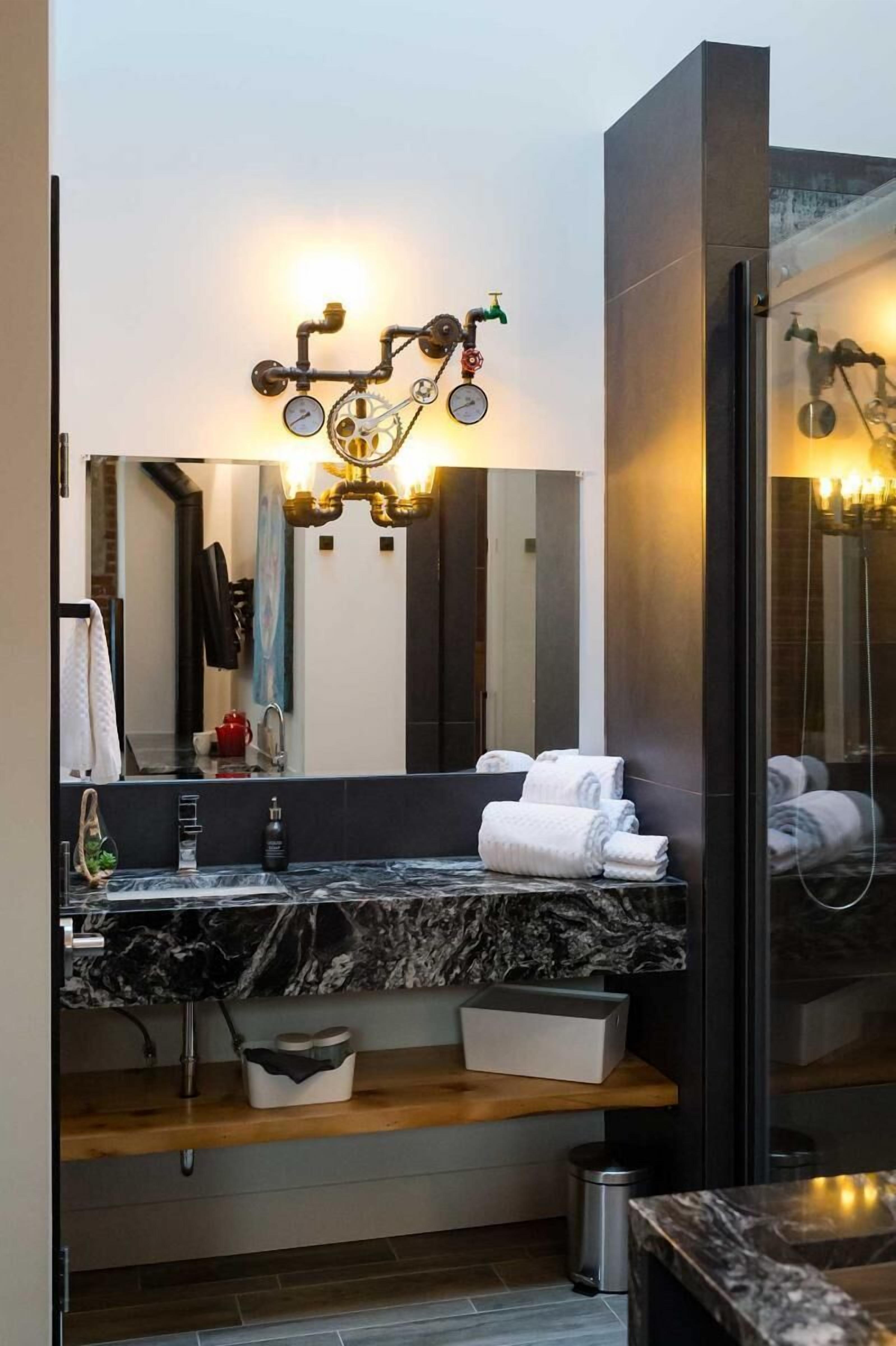 Un baño moderno con lavamanos de mármol, un espejo grande y una lámpara original sobre el espejo.