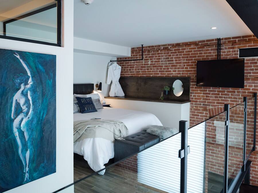 Un dormitorio moderno con pared de ladrillo, un cuadro grande, una cama con cabecero y un televisor montado.