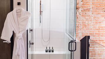 A modern bathroom with a glass-enclosed shower, a white robe hanging on the door, and a brick wall.