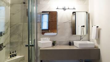 Un baño moderno con ducha envuelta en vidrio, pared de azulejos de mármol, un espejo grande y un lavabo blanco.