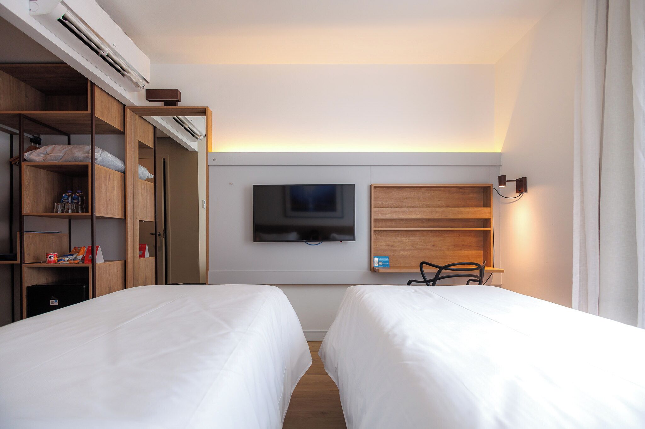 Una habitación de hotel con dos camas, televisión, armario de madera y estante con lámpara.