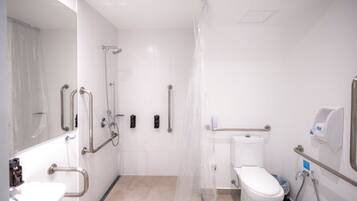 A bathroom with a toilet, sink, shower, and handrails.