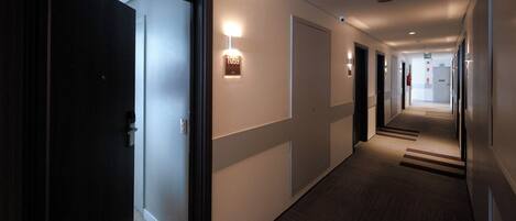 A hotel hallway with doors, light fixtures, and a carpeted floor.