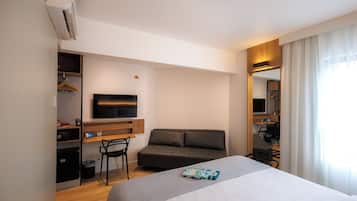A modern hotel room with a bed, a sofa, a desk with a flat-screen TV, a chair, and a wardrobe.