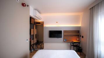 Habitación de hotel con una cama, un televisor montado en la pared, un escritorio con una silla y un equipo de aire acondicionado.