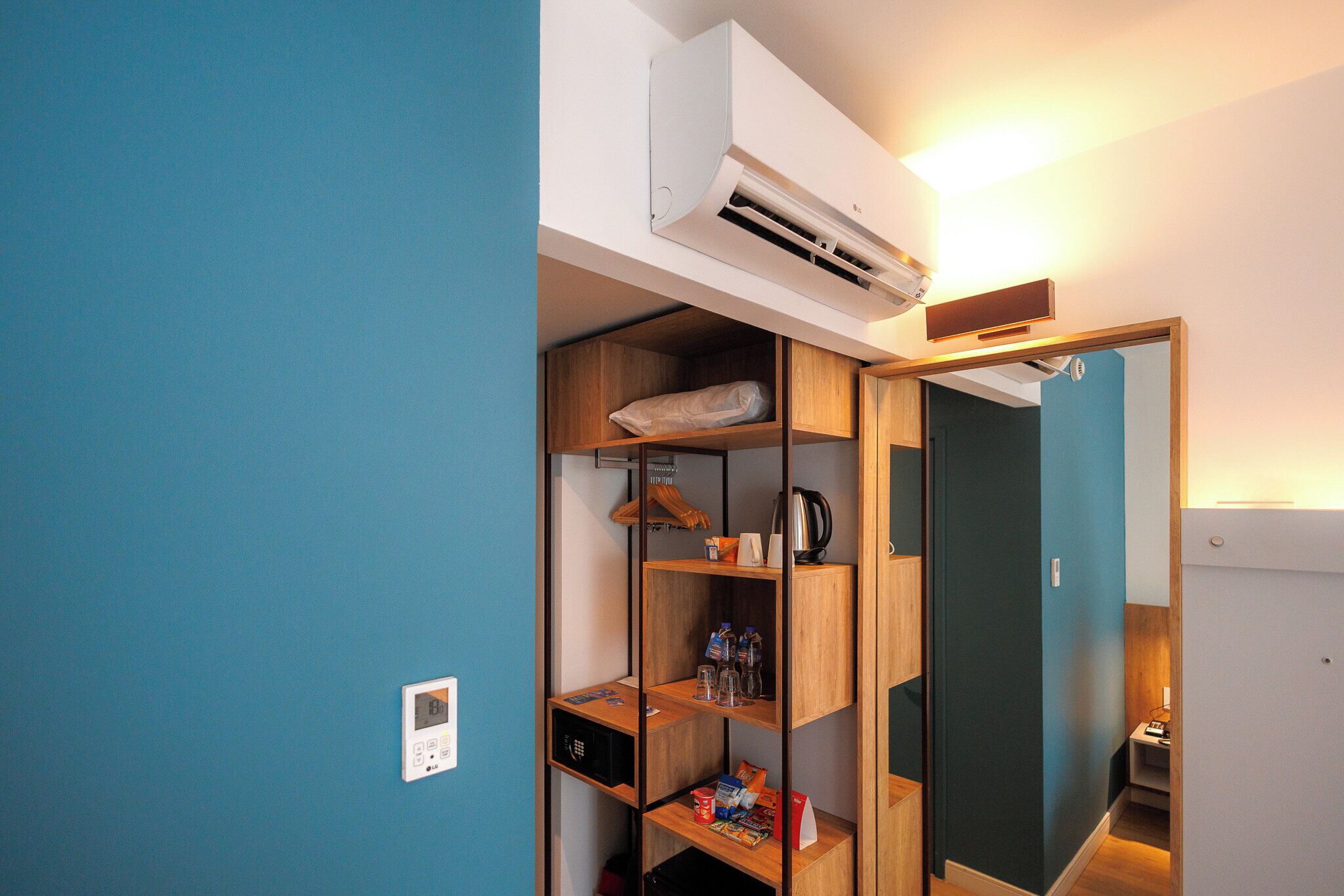 Una habitación con una pared azul, una estantería de madera con varios objetos, un equipo de aire acondicionado y una puerta que da a otra habitación.