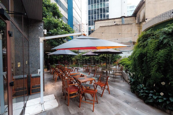 Un espace extérieur aménagé avec des tables et des chaises, entouré de verdure et bordé par un bâtiment.