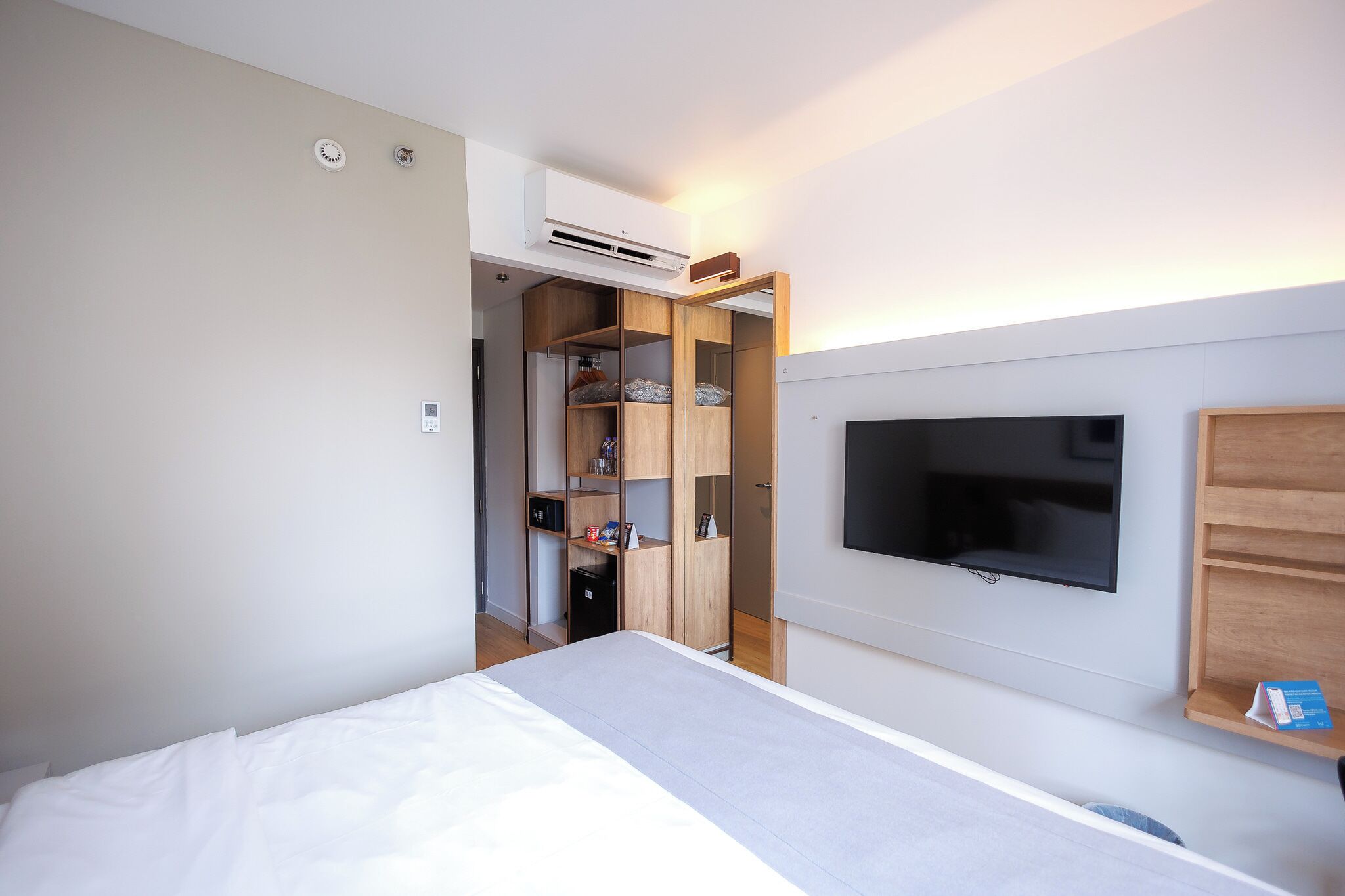 A bedroom with a bed, a TV mounted on the wall, and a wooden wardrobe.