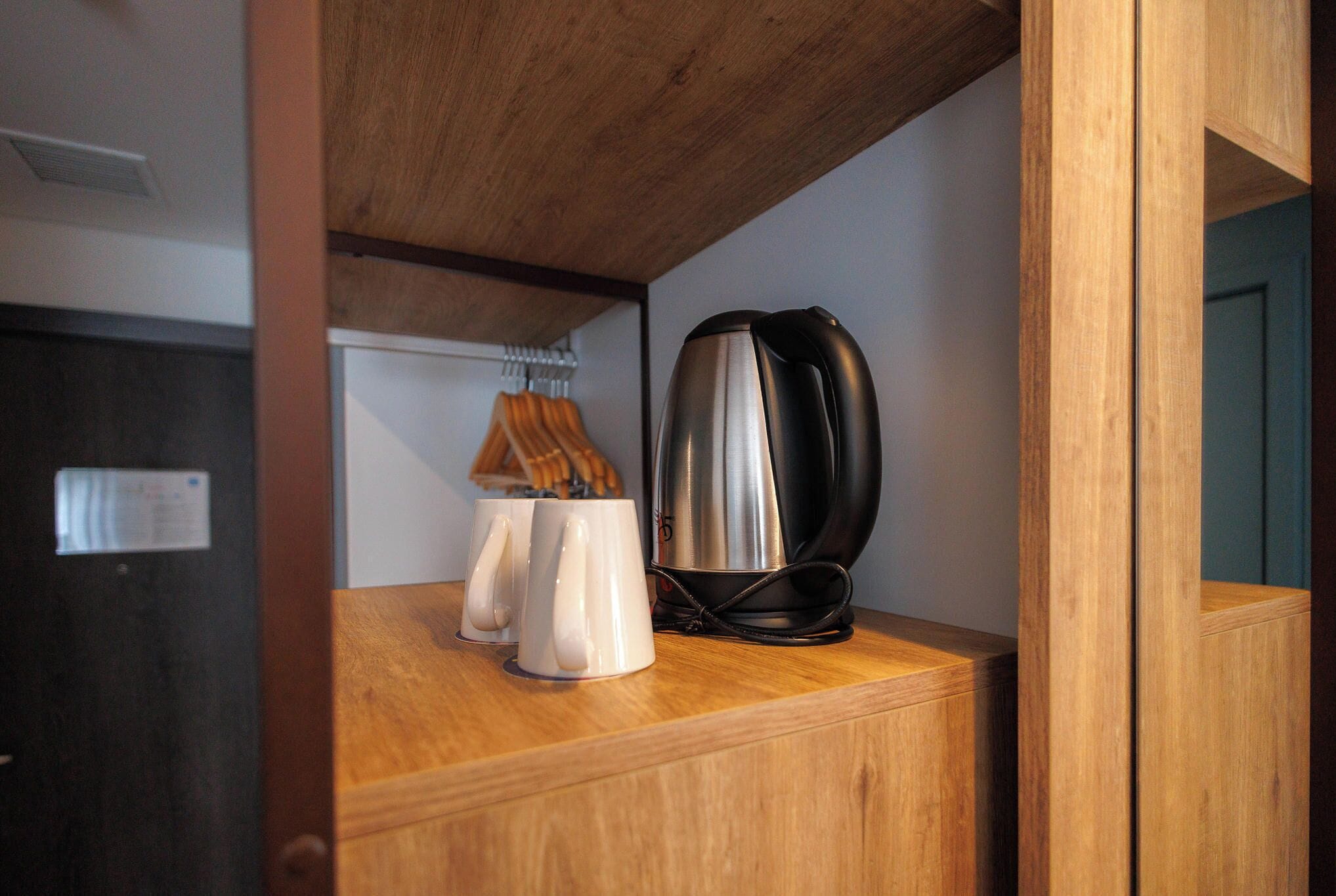 Een houten plank met een waterkoker, twee witte mokken en een hangende lamp.