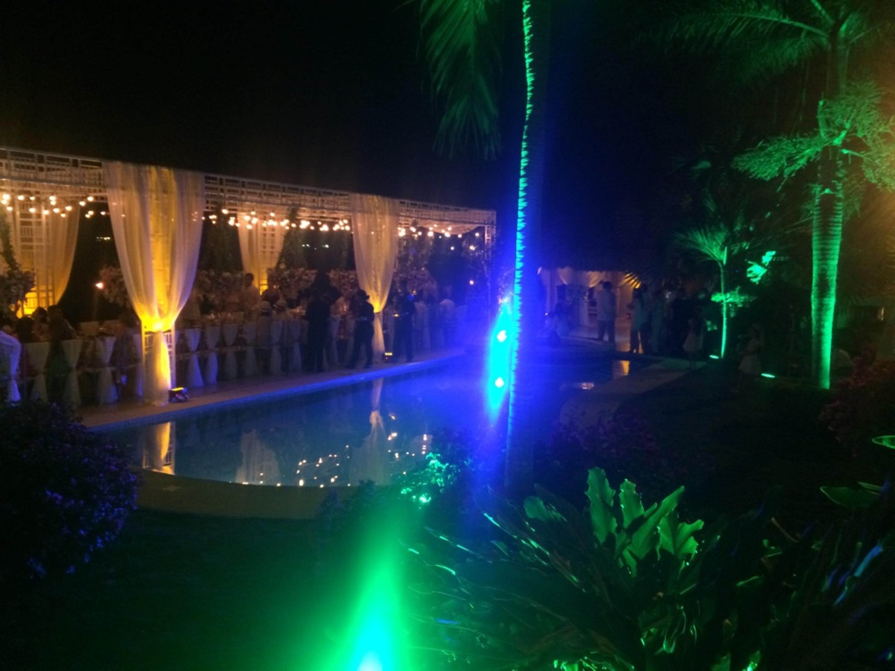 Evento nocturno al aire libre con piscina, cortinas blancas y una iluminación ambiental.