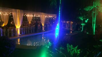 Evento nocturno al aire libre con piscina, cortinas blancas y una iluminación ambiental.