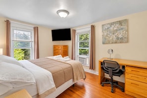 A hotel room with a bed, a desk, a chair, a television, and a window with curtains.