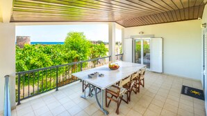 A covered balcony with a table and chairs, a view of the sea, and a door with shutters. - Villa Euphoria (Rhodes)