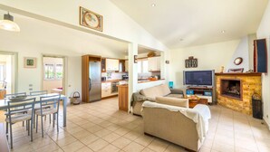 A spacious living room with a sofa, TV, fireplace, and kitchen in the background. - Villa Euphoria (Rhodes)