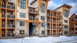 A multi-story hotel with a stone facade, wooden balconies, and a sign indicating it is a lodge. - Spacious Mountain View Retreat | Prime Location (Canmore)