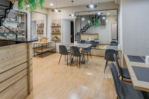 A modern restaurant with wooden flooring, black chairs, and a staircase leading to a loft area.