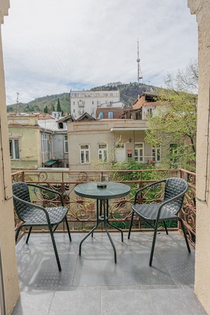A balcony with two chairs and a table, overlooking a residential area with buildings and a tower.