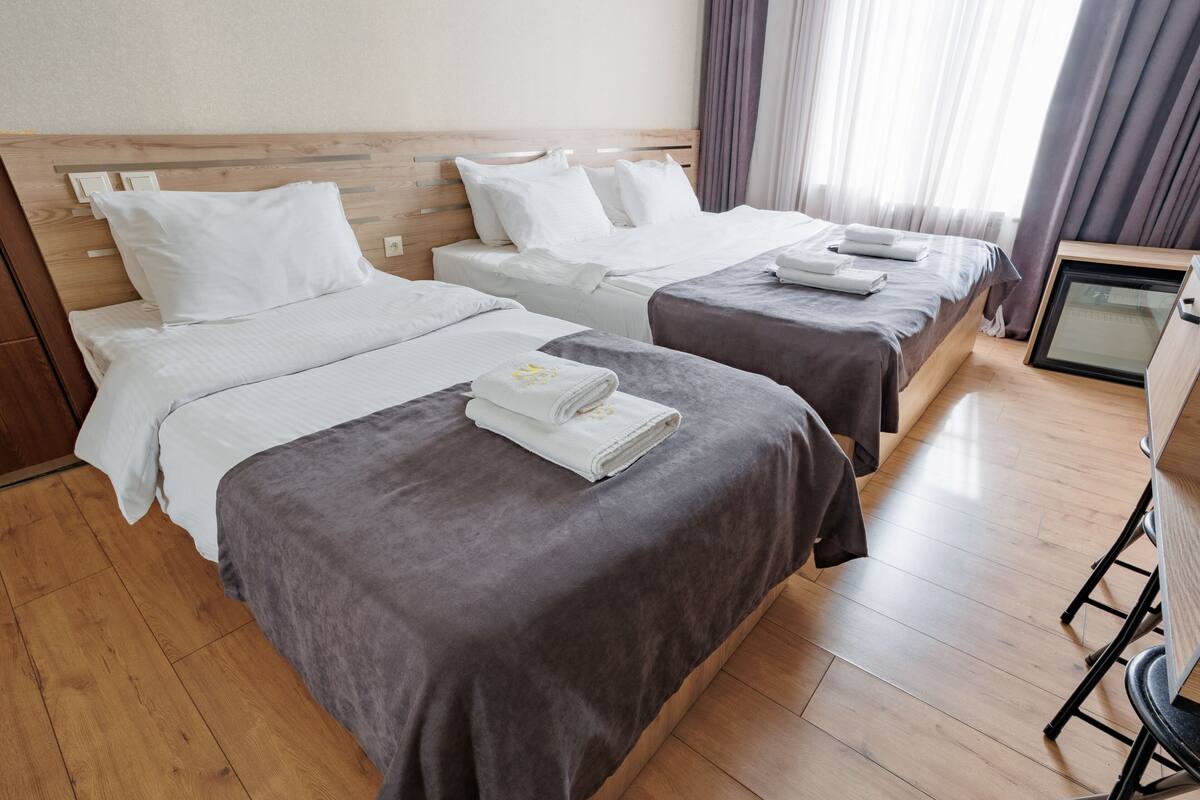 A hotel room with two beds, wooden headboards, and a small desk with a chair.