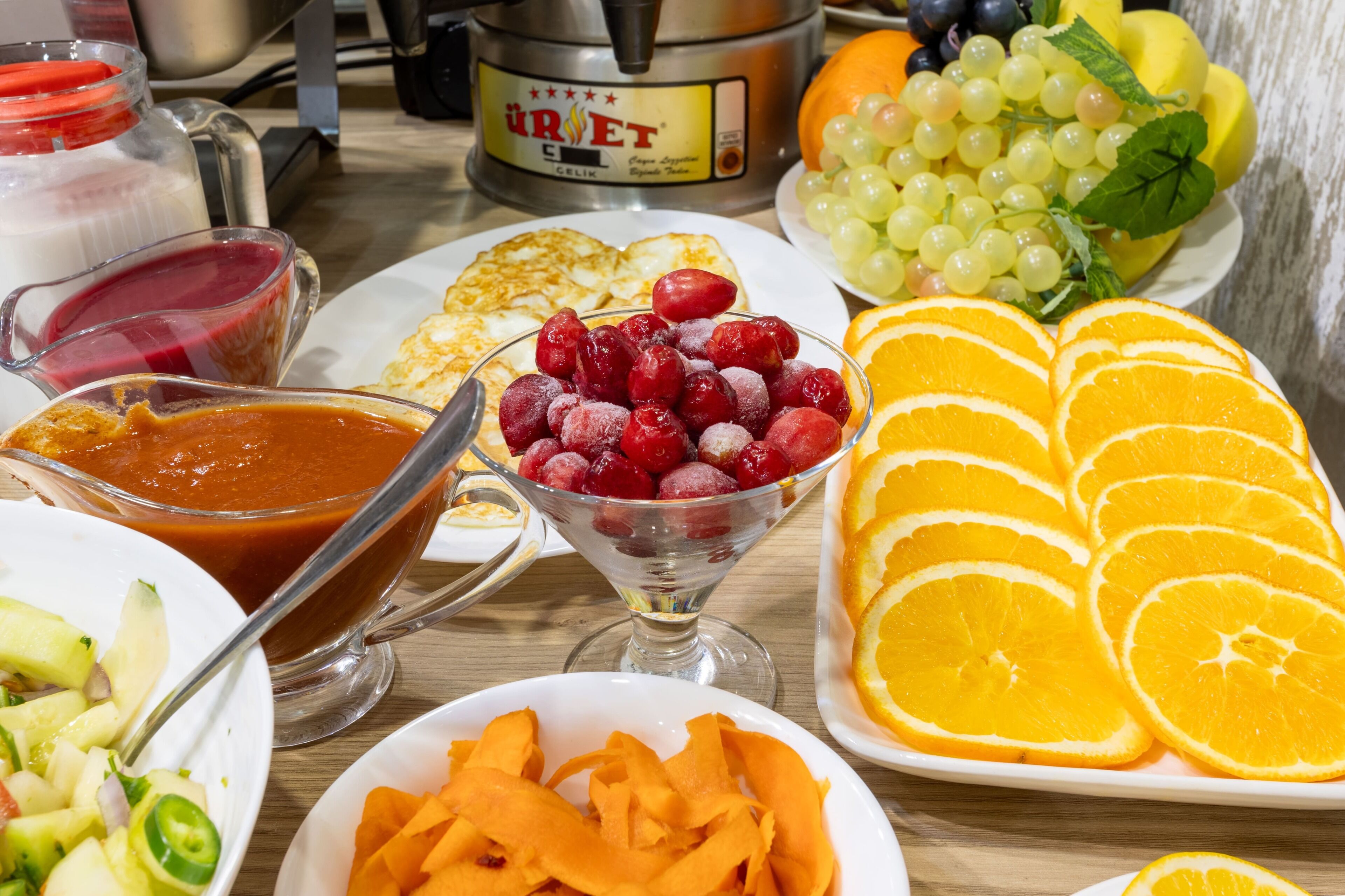 A breakfast spread with various fruits, a coffee maker, and a glass of juice.
