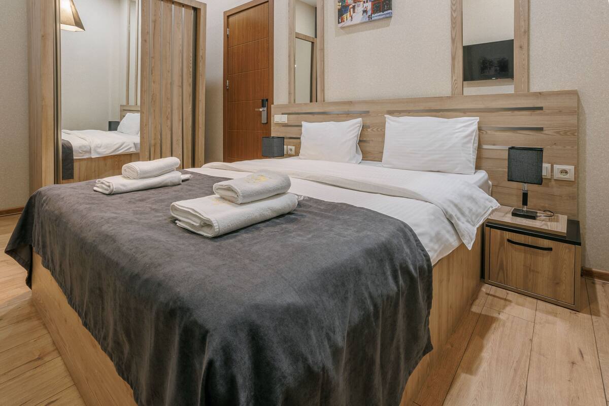 A hotel room with a wooden bed, a nightstand, a mirror, and a wall-mounted TV.