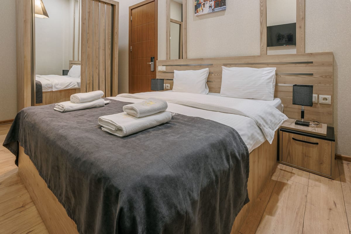 A hotel room with a bed, bedside tables, a mirror, and a wooden floor.