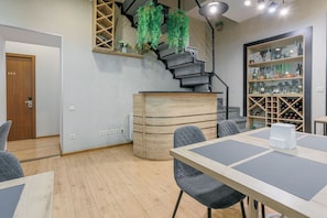 A modern interior with a staircase, a wooden cabinet, a dining area with tables and chairs, and a wine rack.