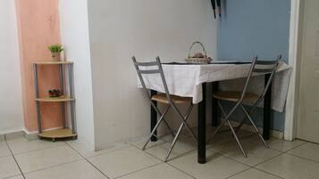 Un comedor con una mesa dispuesta para dos, una silla de metal, un estante con planta en maceta y una cesta sobre la mesa.
